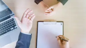 Két ember megbeszélése egy irodai asztalnál laptop és jegyzetlap mellett