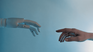 Egy emberi kéz és egy robotkéz közeledik egymáshoz egy kék háttér előtt, szimbolizálva az ember és az automatizált technológia kapcsolatát.