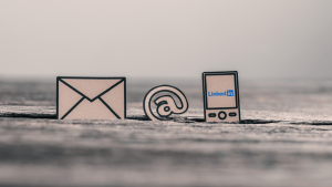 Papír ikonok e-mailről, @ jellel és mobilon megjelenő LinkedIn logóval, a LinkedIn jelenlét fontosságát és a digitális kapcsolatépítést jelképezve.