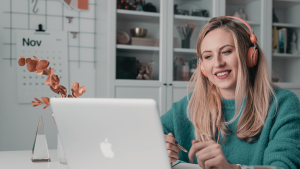 A fiatal nő diákmunka közben, fejhallgatóval a fókuszált munkájára koncentrál a laptopján.